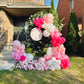 Balloon arch with pink, white, and red balloons in front of a house.