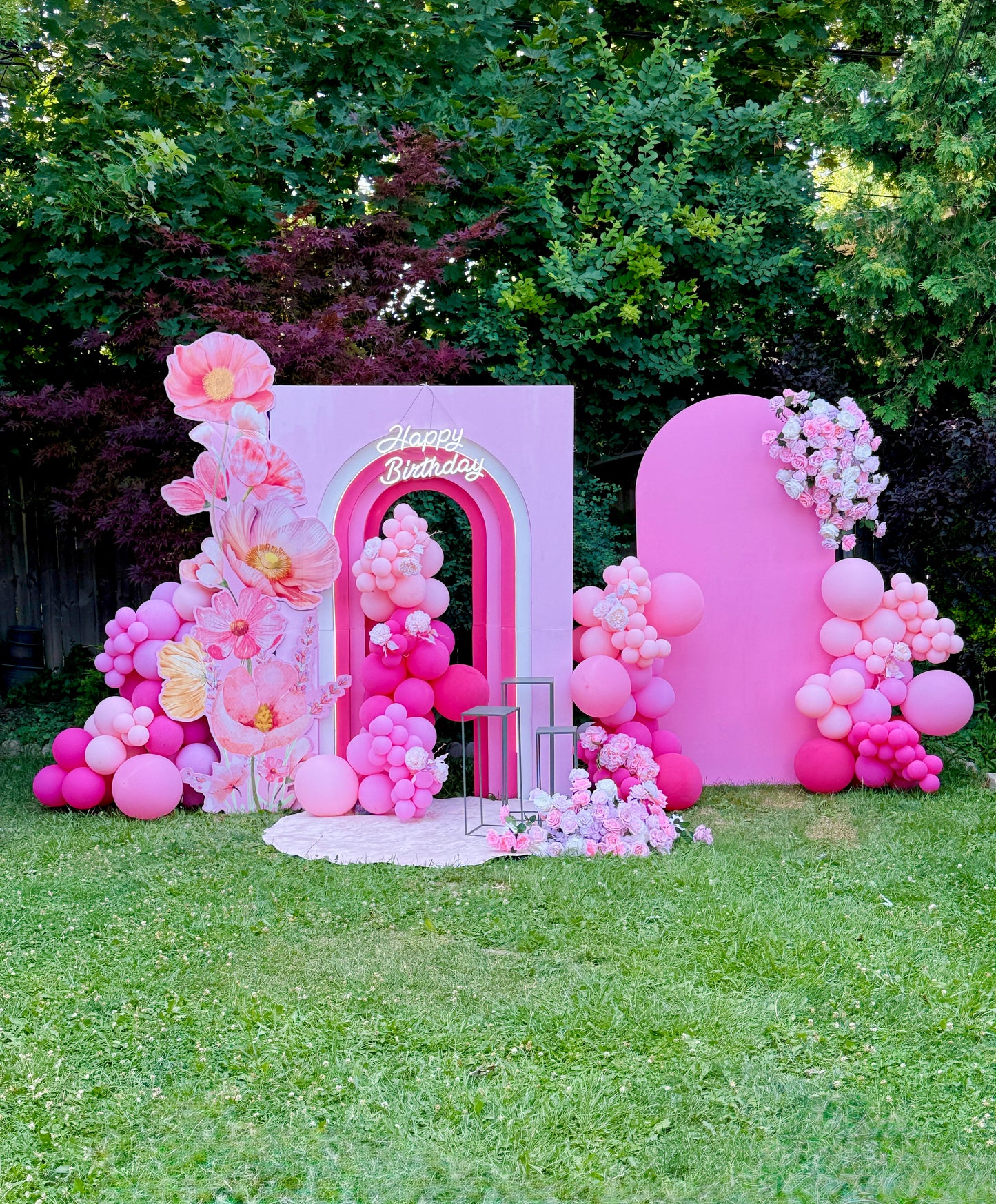 Pink birthday arch with balloons and flowers in a garden setting