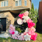 Balloon arch with pink, white, and gray balloons in front of a house.