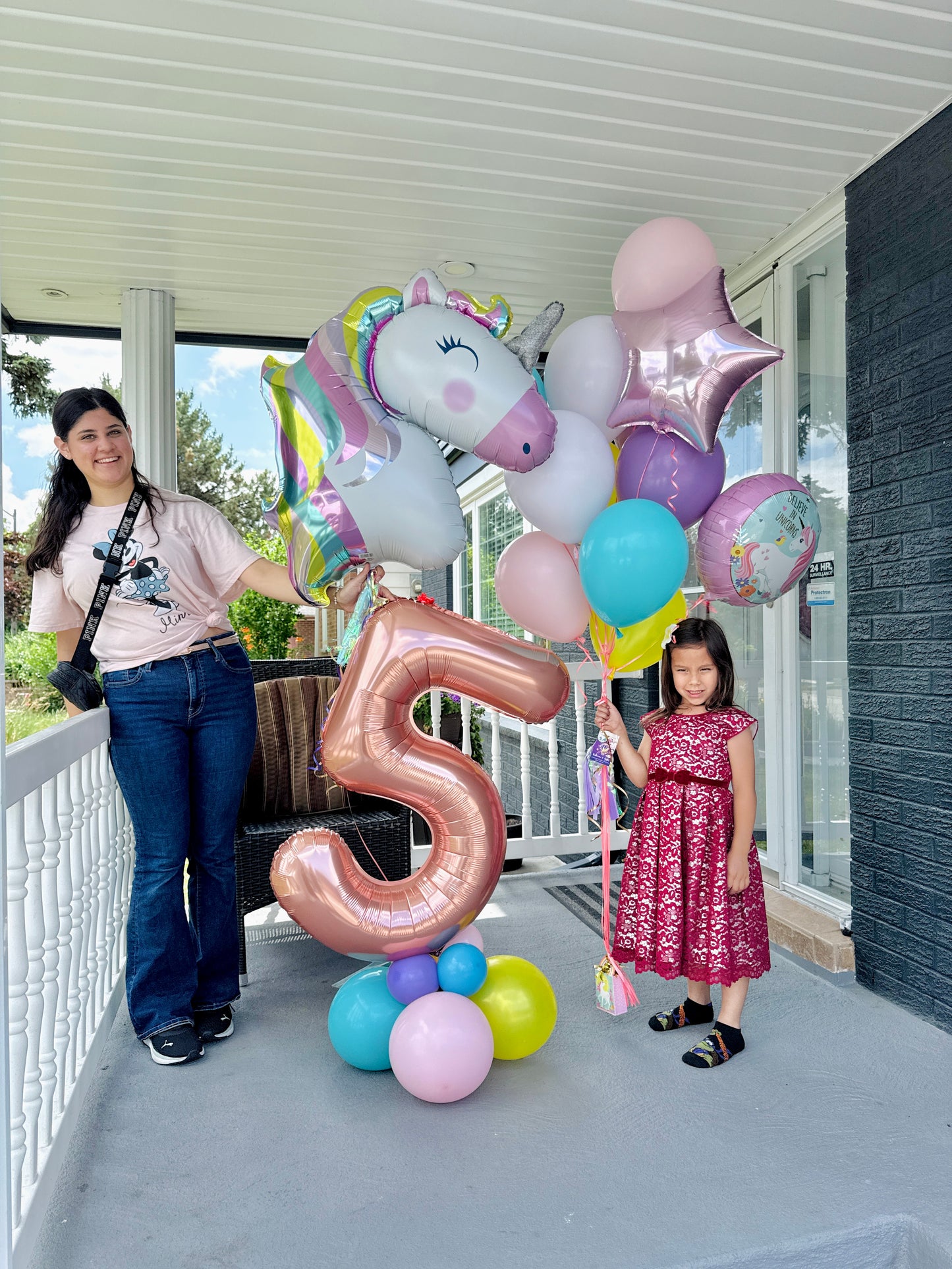 Woman and child with balloons and a large number '5' on a balcony