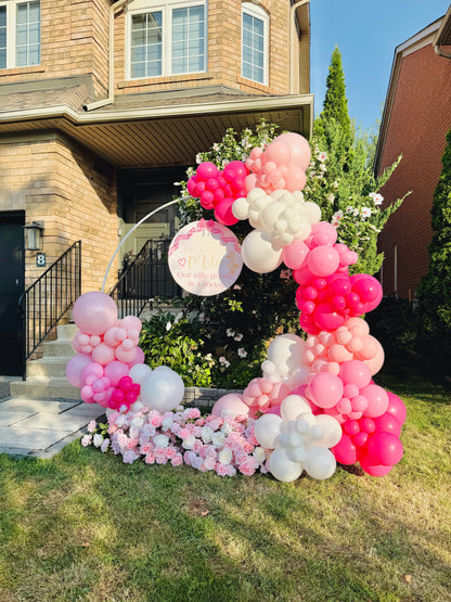 Balloon arch with pink, white, and red balloons in front of a house.
