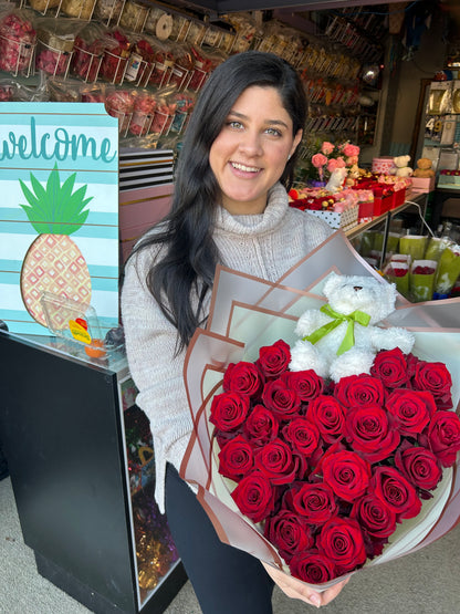 Heart-shaped bouquet of fresh red roses wrapped in floral paper with a teddy bear included.