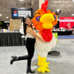 Person posing with a large balloon rooster sculpture at an event.