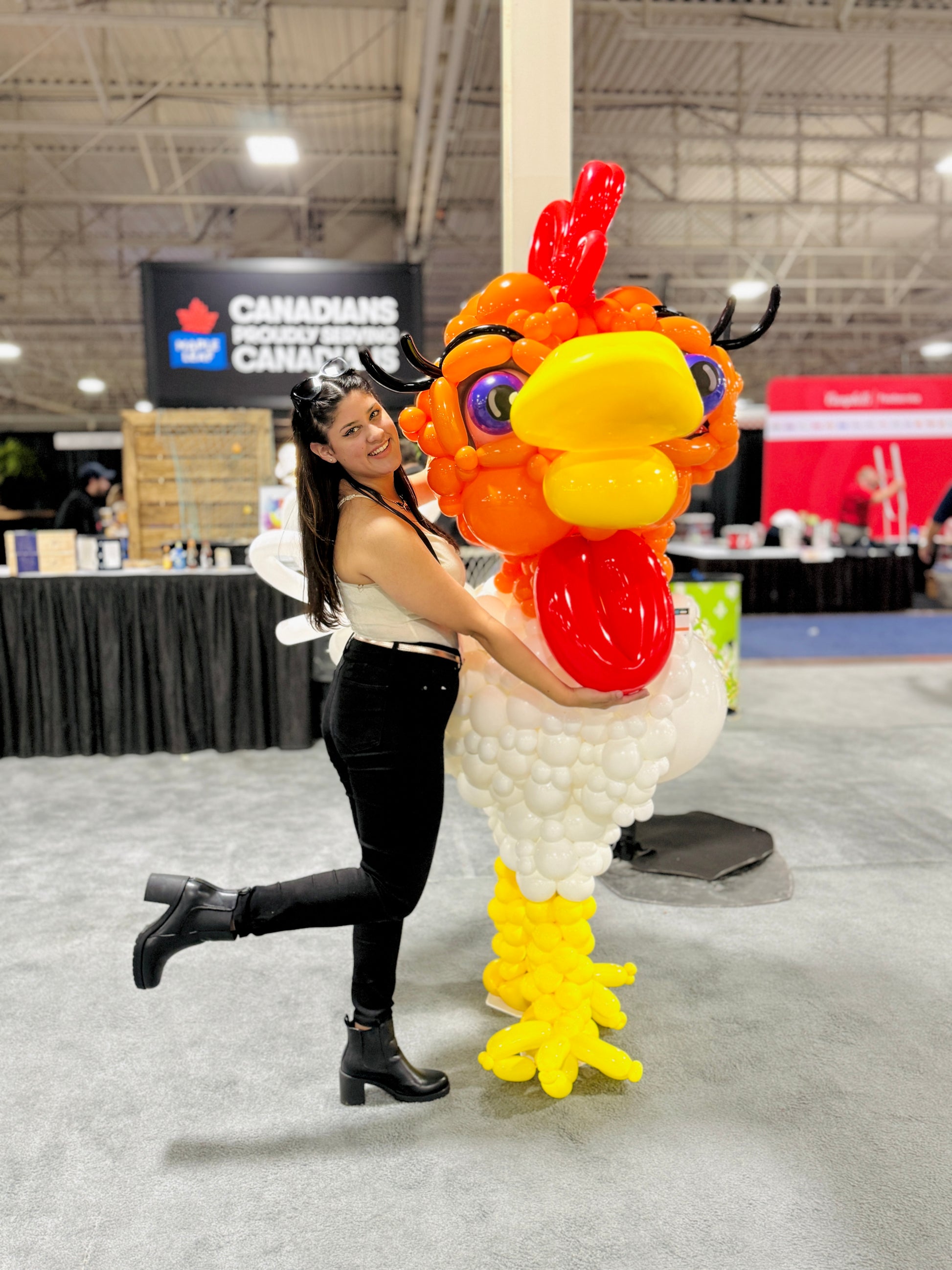 Person posing with a large balloon rooster sculpture at an event.
