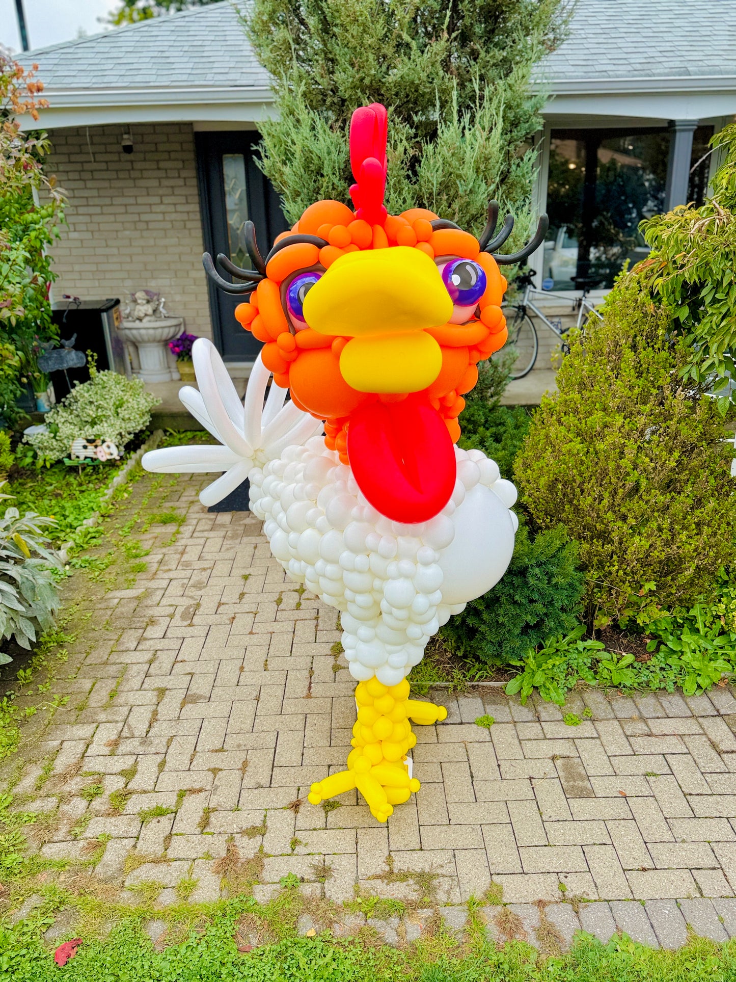 Balloon sculpture of a rooster in front of a house
