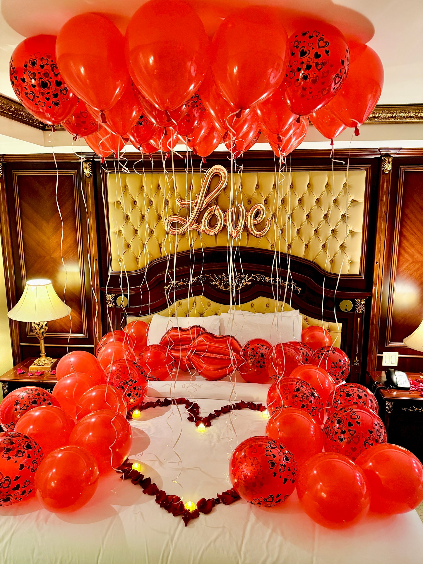 Decorative setup with red balloons and a heart-shaped arrangement on a bed, featuring the word 'Love'.