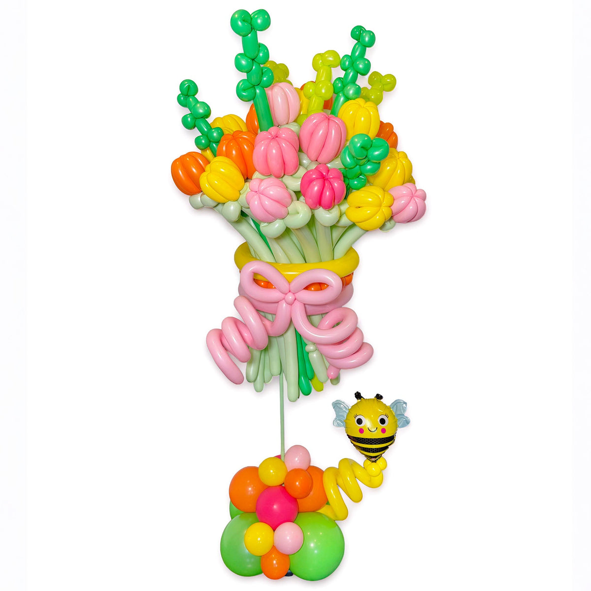 A colorful balloon bouquet decoration with pink, yellow, orange, and green balloons, tied with a pink balloon bow, and a small yellow-and-black bee balloon figure beside it on a plain white background.