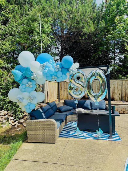 Outdoor setting with blue and white balloons and a '80' balloon in a garden.