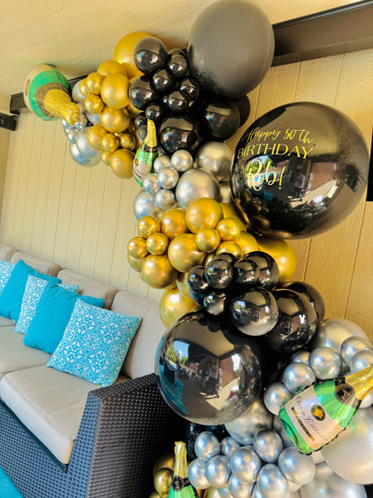 Balloon arch with gold, black, and silver balloons in a living room setting.