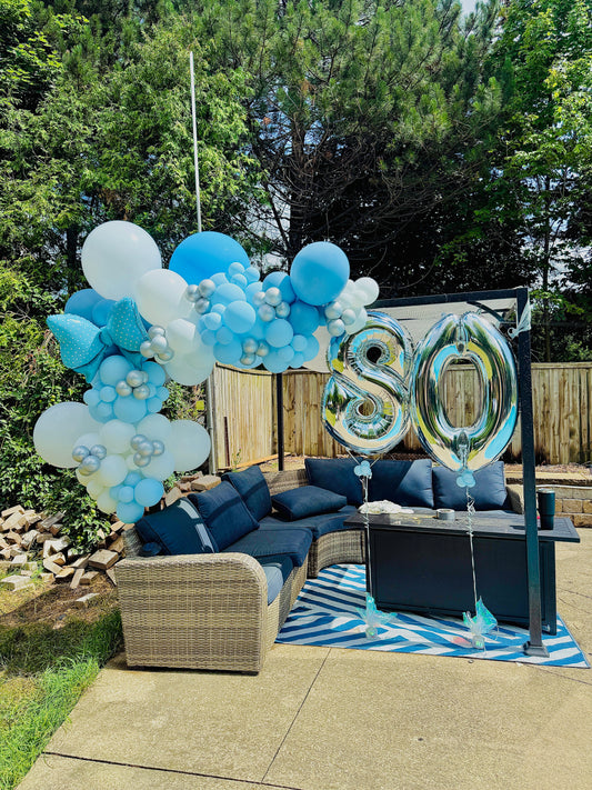 Outdoor setting with blue and white balloons and '80' balloons on a patio.