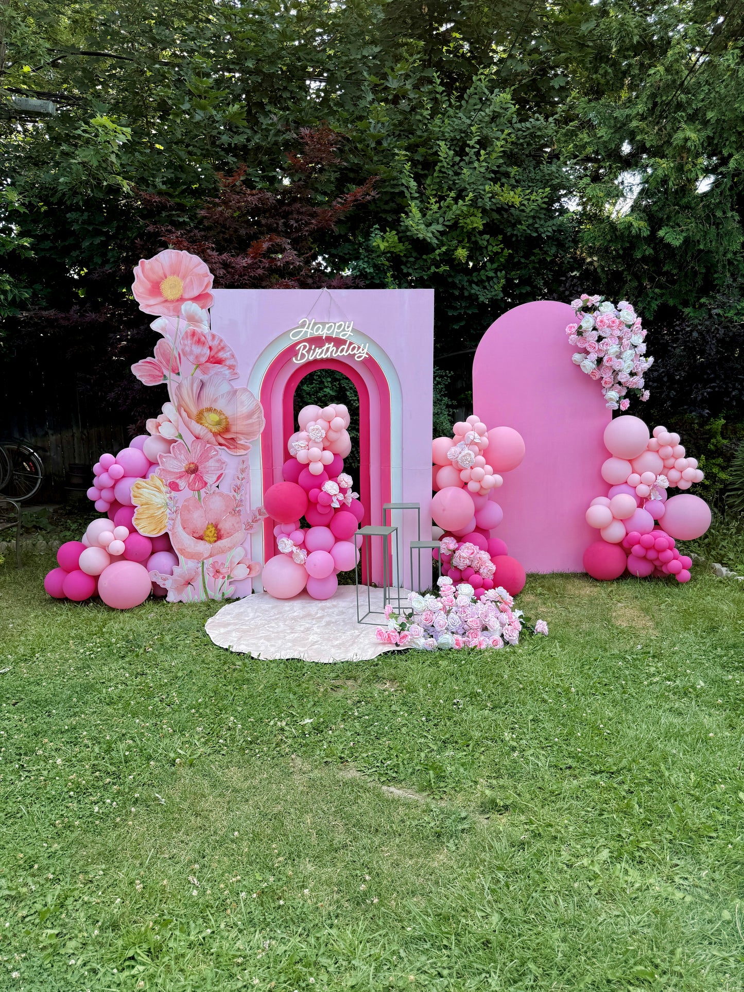 Decorative birthday arch with pink balloons and flowers on a grassy area