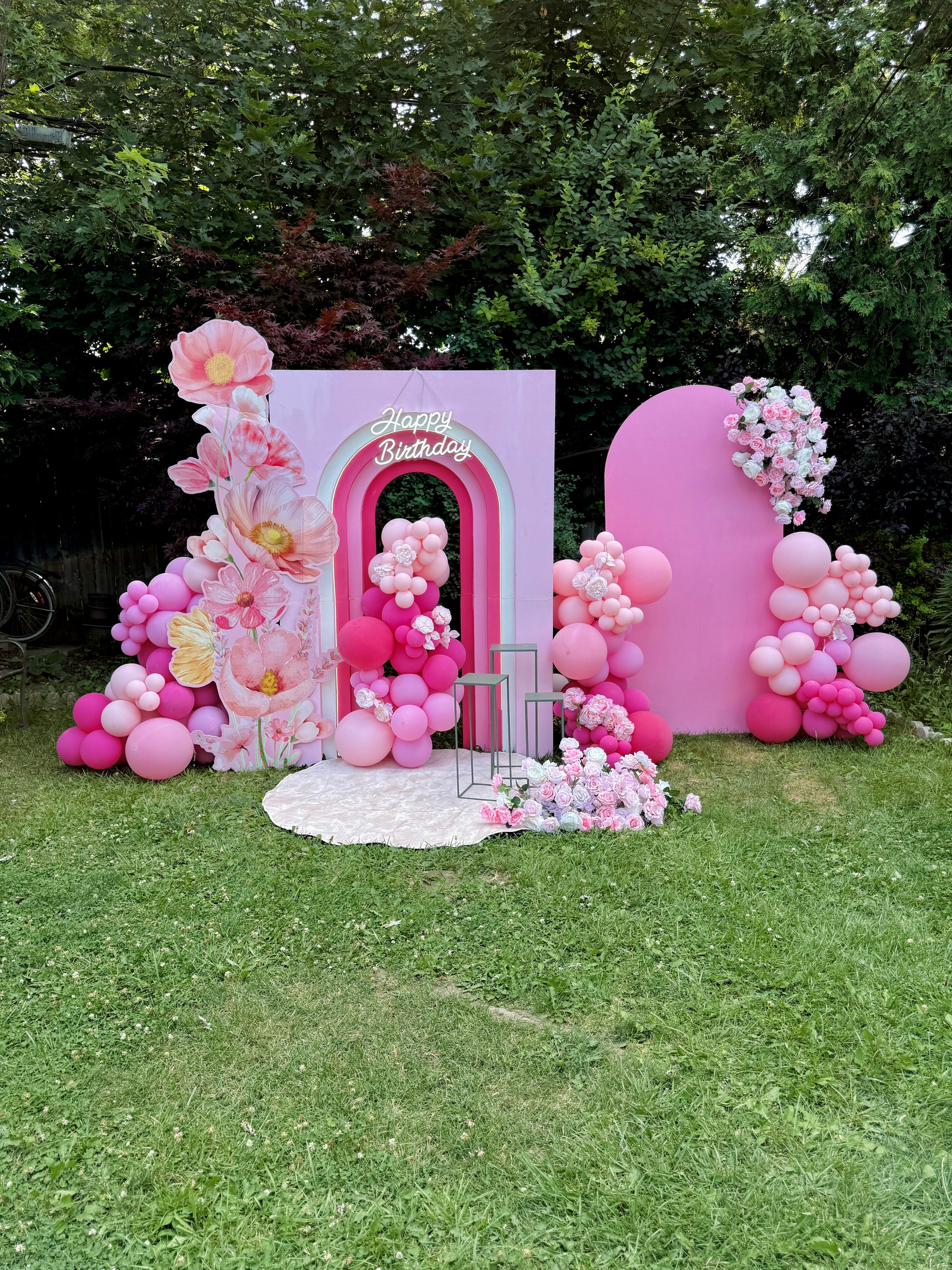 Decorative birthday arch with pink balloons and flowers on a grassy area