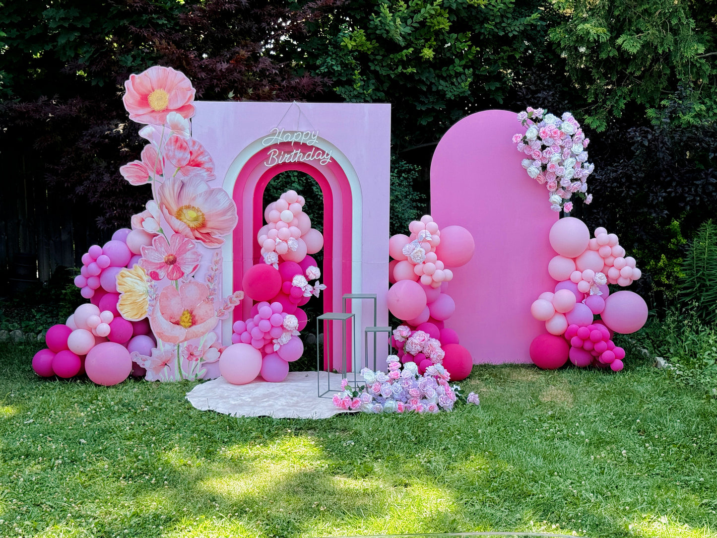 Decorative arch with pink balloons and flowers in a garden setting