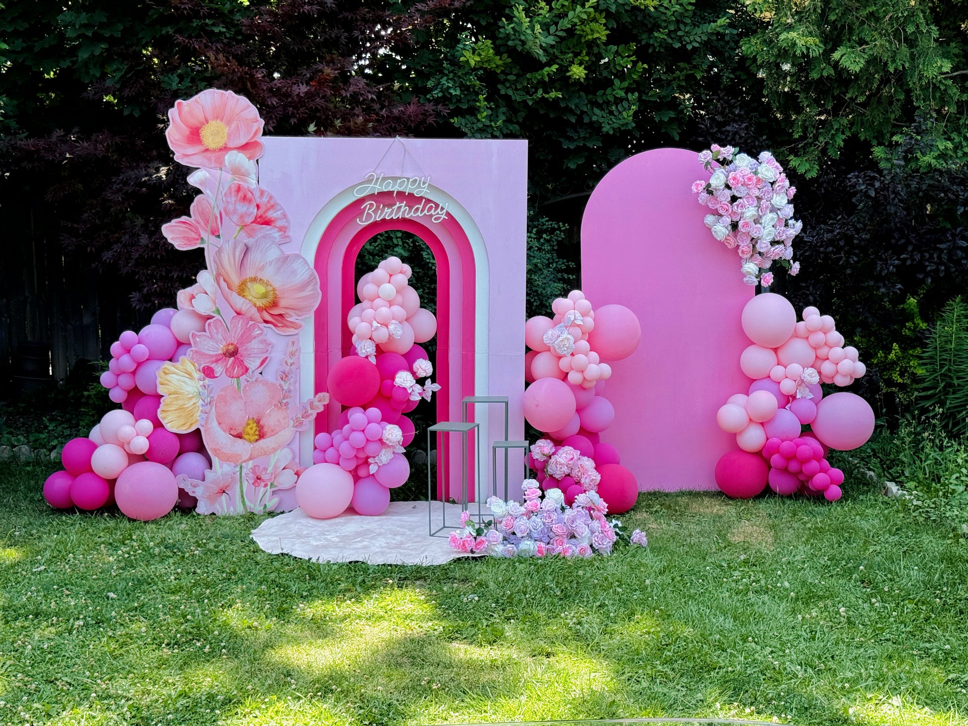 Decorative arch with pink balloons and flowers in a garden setting