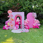 Decorative arch with pink balloons and flowers on a grassy area