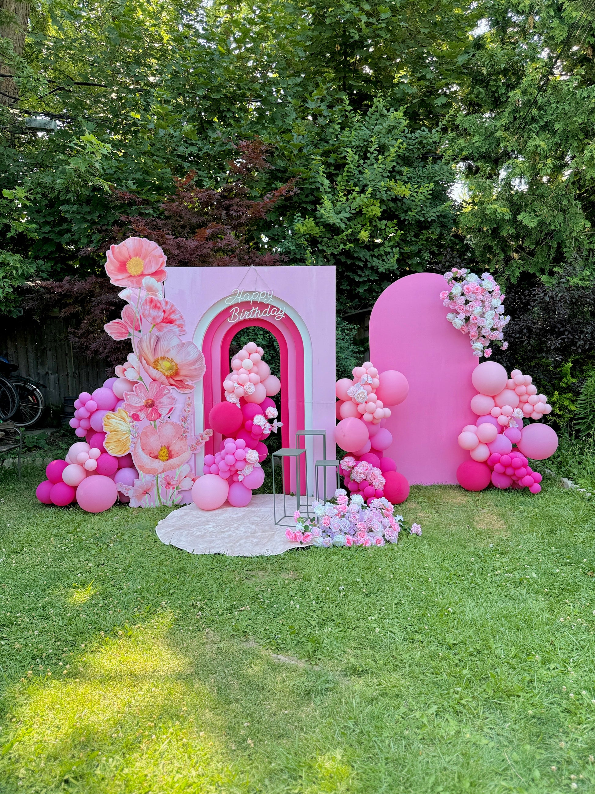 Decorative arch with pink balloons and flowers on a grassy area