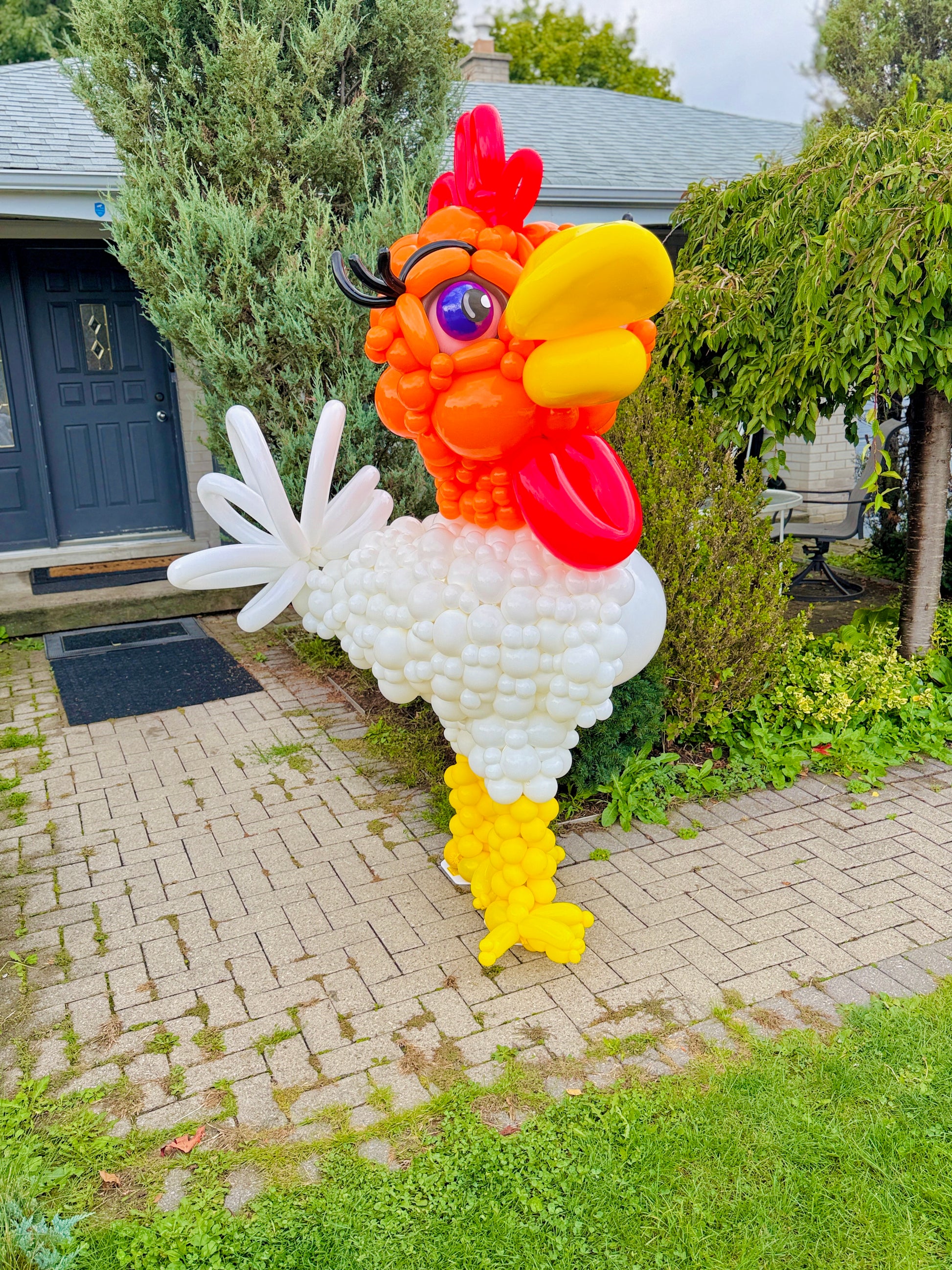 Balloon sculpture of a rooster in front of a house