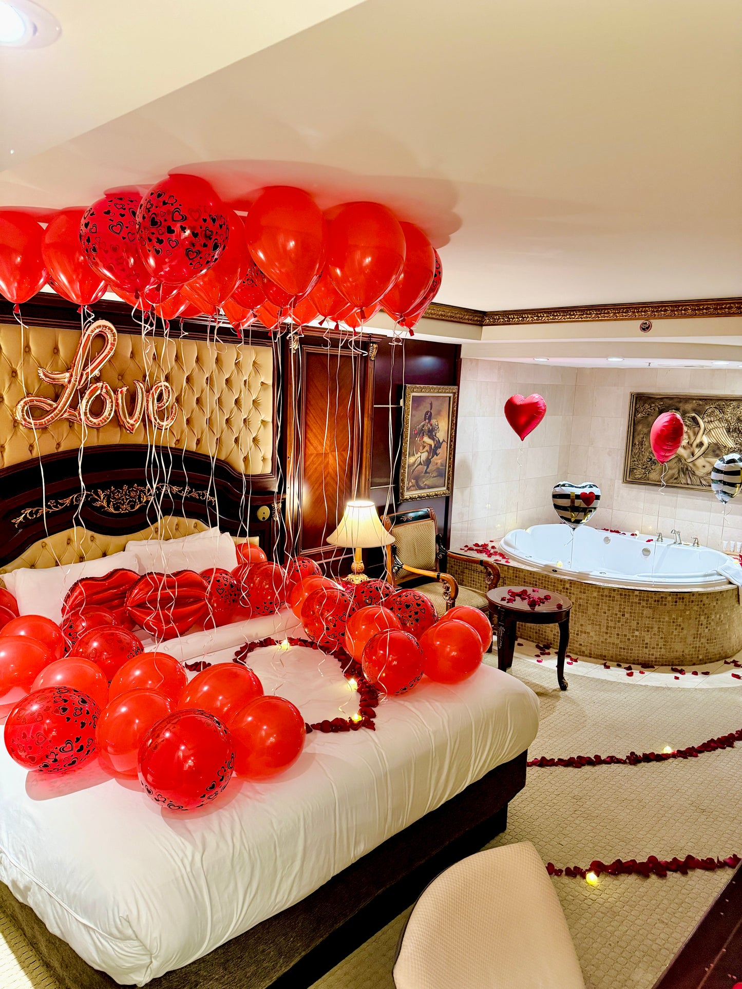 Decorated bedroom with red balloons, 'Love' sign, and a jacuzzi.