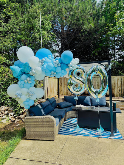 Outdoor setting with blue and white balloons and '80' balloons on a patio.