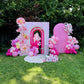 Decorative arch with pink balloons and floral arrangements on a grassy area