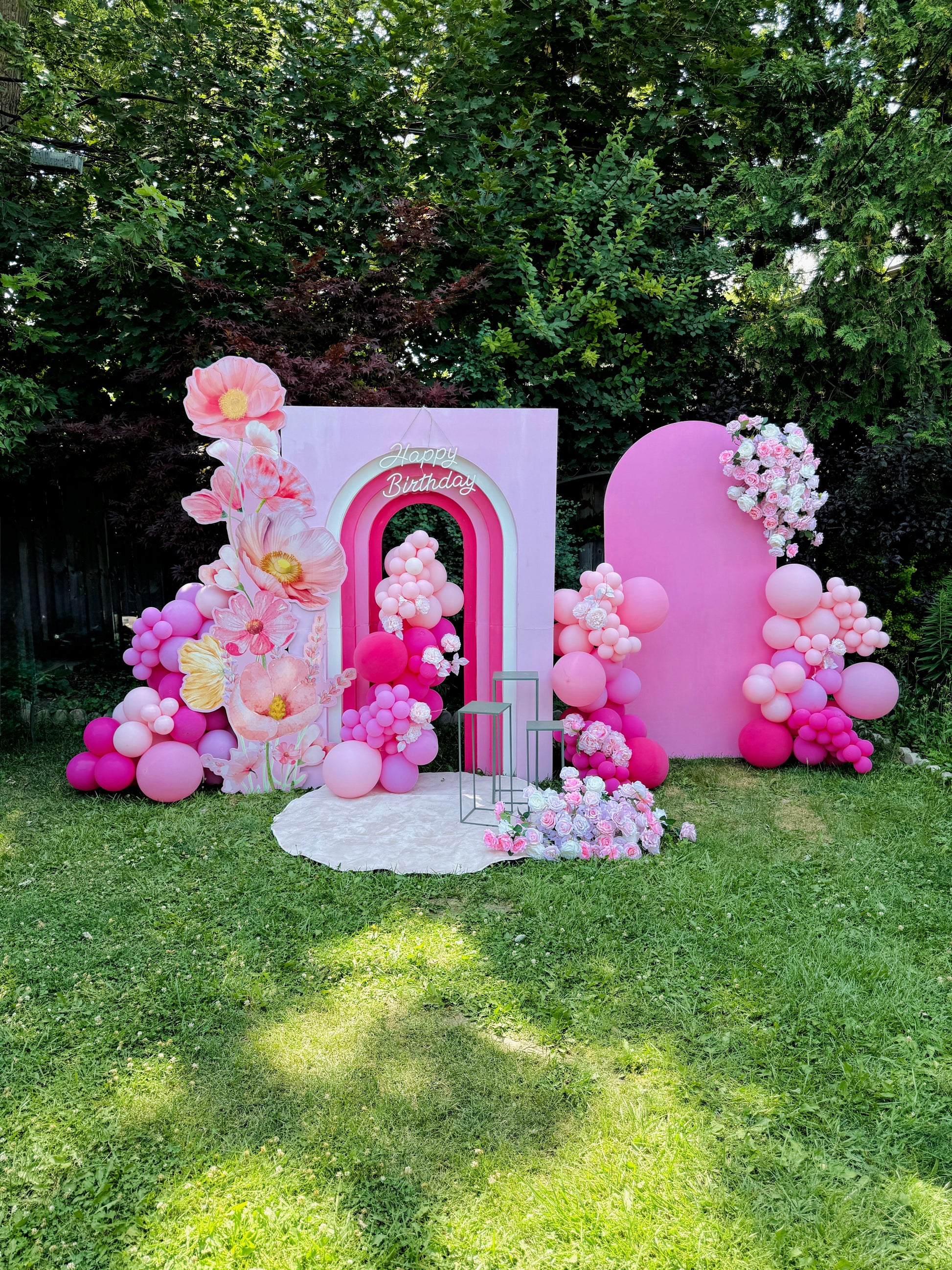 Decorative arch with pink balloons and floral arrangements on a grassy area