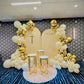 Decorative arch with balloons and a cross on a patterned wall.