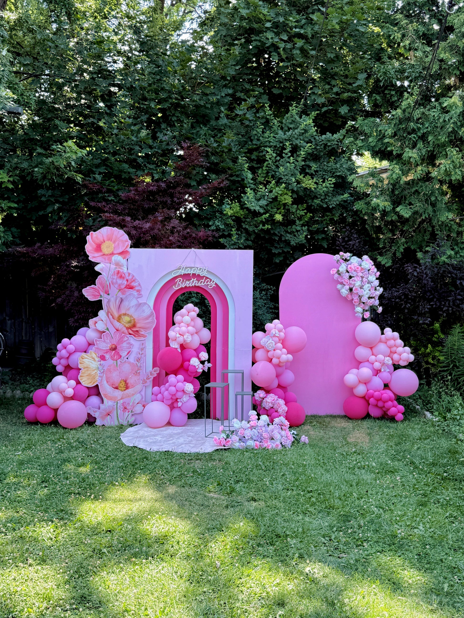 Decorative arch with pink balloons and floral arrangements in a garden setting