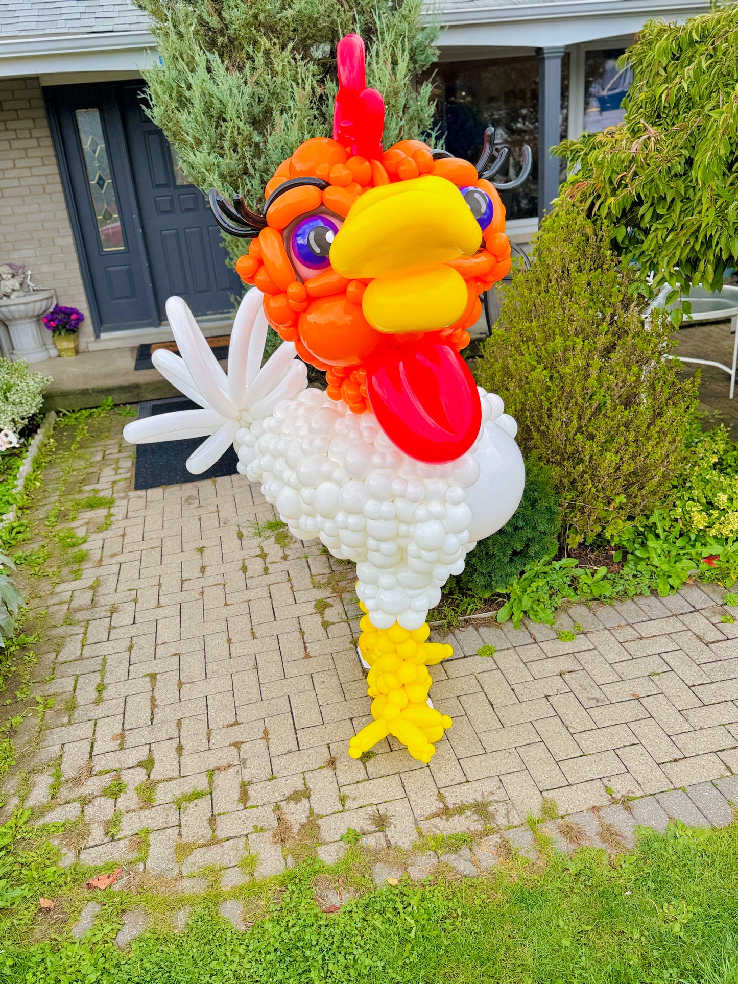 Balloon sculpture of a rooster in front of a house
