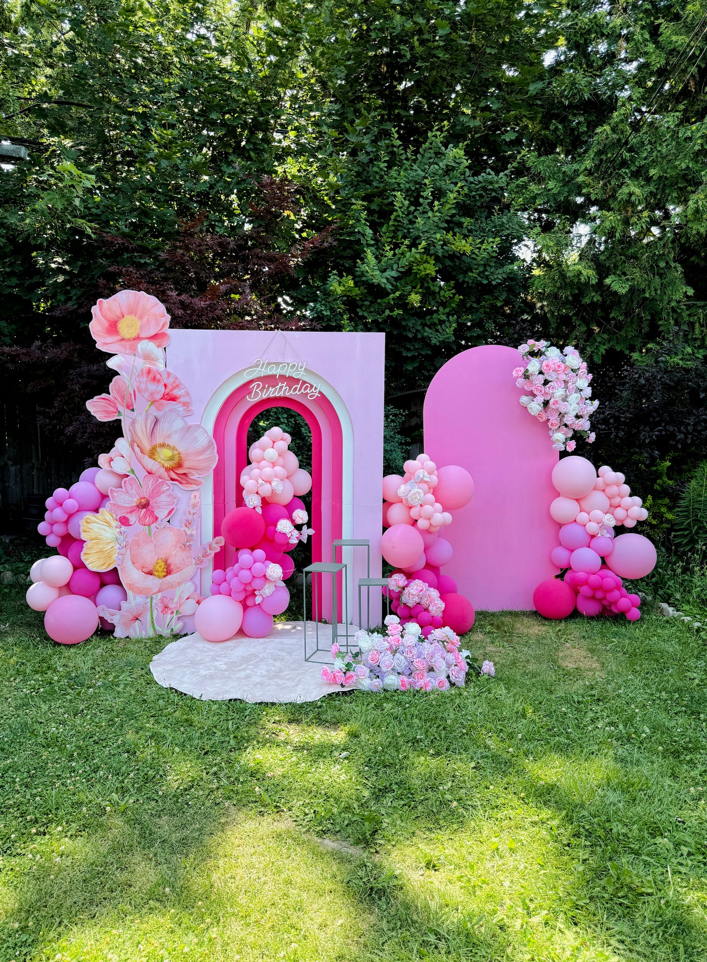 Decorative archway with pink and white balloons and flowers in a garden setting