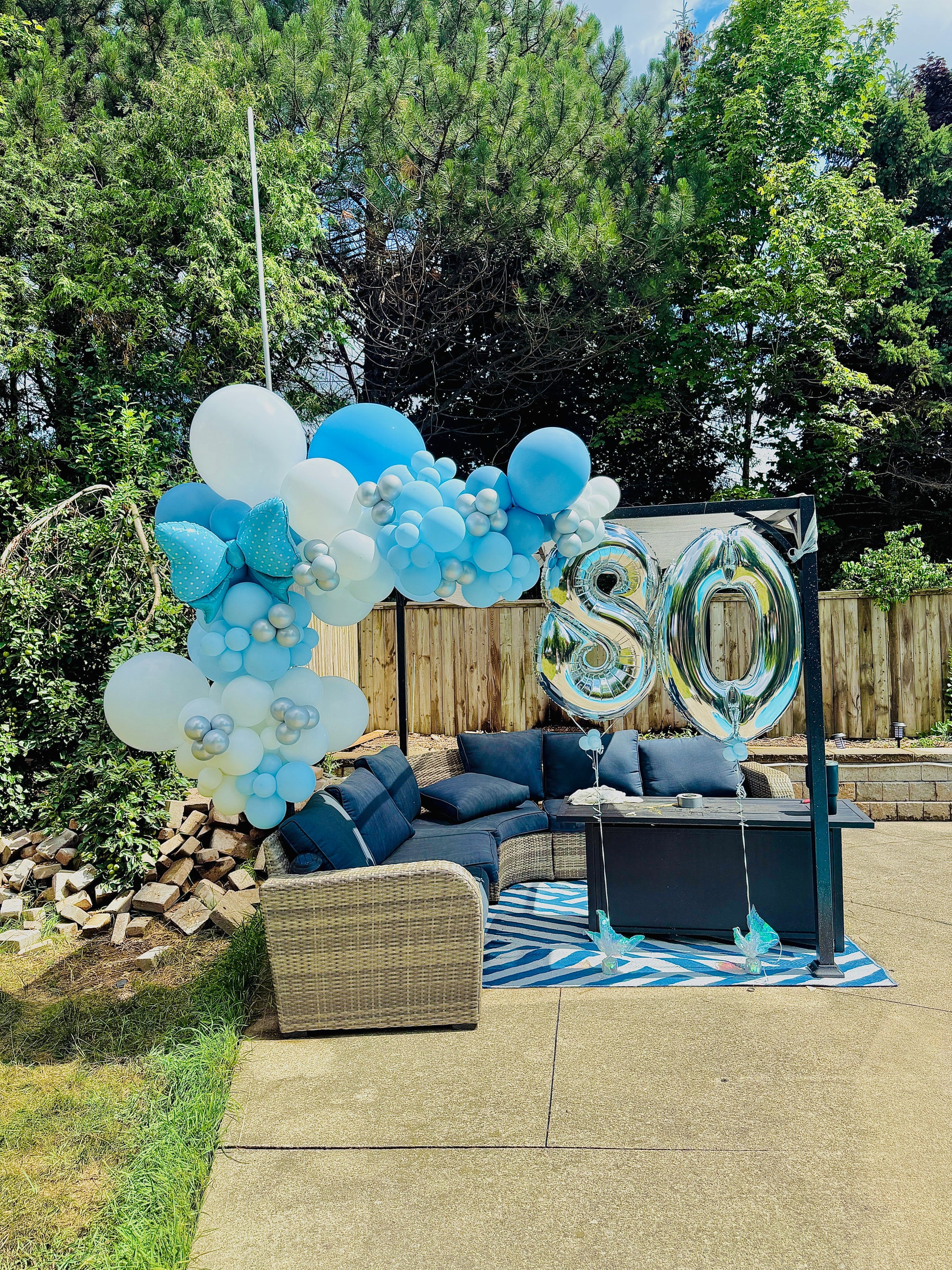 Outdoor setting with blue and white balloons and a '80' sign in a garden.