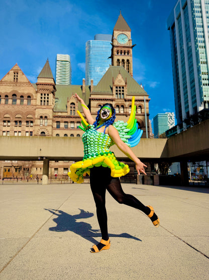 Person in a colorful costume dancing in an urban setting with tall buildings in the background