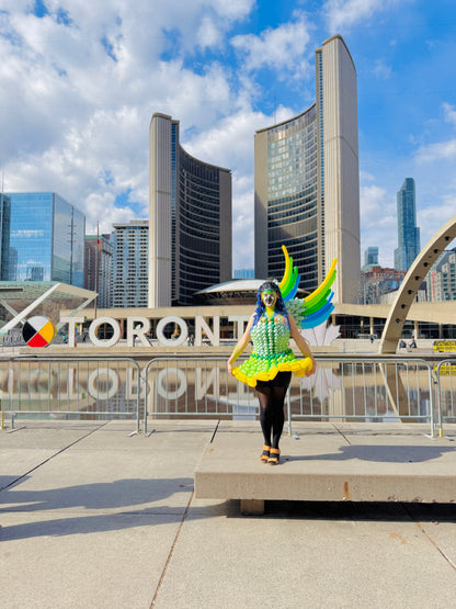 Person in colorful outfit standing in front of the Toronto City Hall with a blue sky.