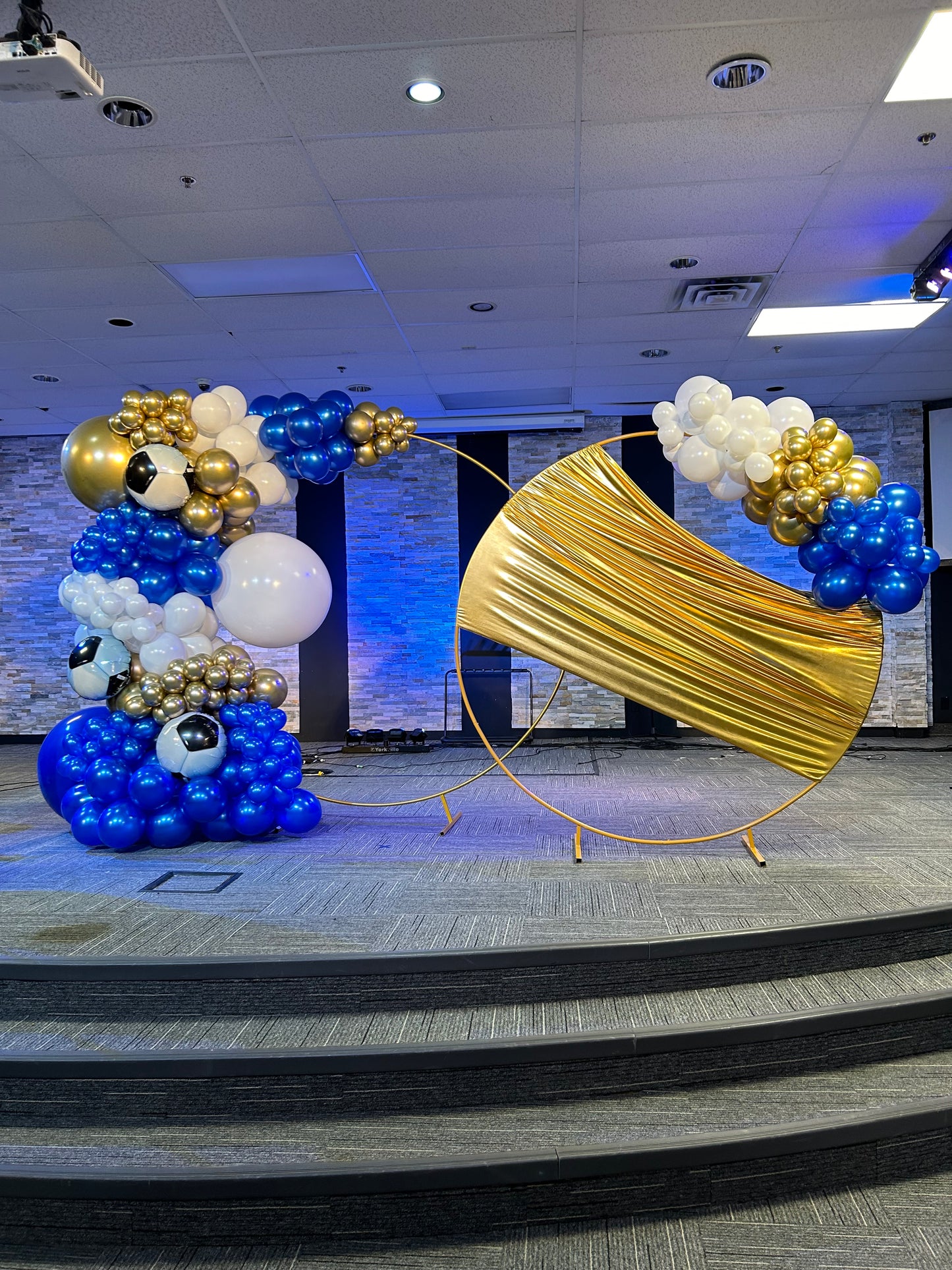 Luxury Soccer Balloon Backdrop with a gold arch, blue and white balloon arrangement, and soccer-themed decorations for a sports event.