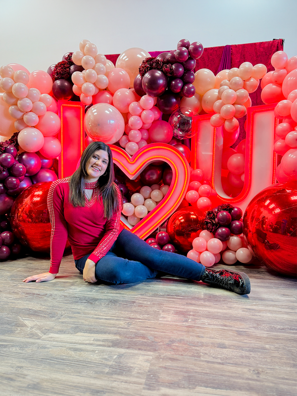 Romantic event decor featuring an illuminated 'I ❤️ U' sign, elegant red and blush balloons, and floral embellishments.