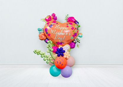 Mother’s Day balloon stand with heart balloon, lavender twisting shapes, mini flowers, and hand-styled balloon base