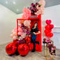 Romantic red phone booth balloon setup featuring blush, burgundy, and red balloons with floral accents. A couple sits inside, creating a cozy and elegant atmosphere.