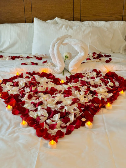 Heart made of fresh rose petals on bed with swan towels – romantic hotel decor in Toronto