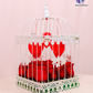 Lovebird Rose Cage with fresh red roses inside a vintage-inspired white birdcage with heart decorations.