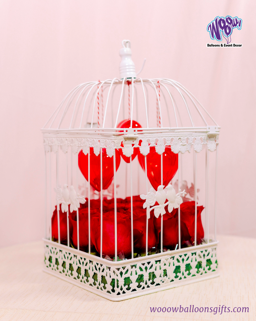 Lovebird Rose Cage with fresh red roses inside a vintage-inspired white birdcage with heart decorations.