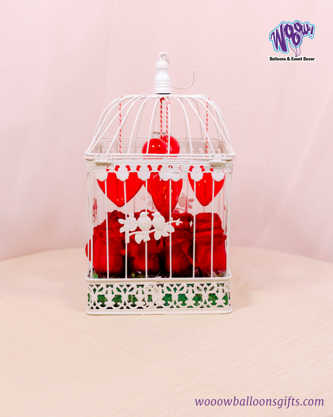 Lovebird Rose Cage with fresh red roses inside a vintage-inspired white birdcage with heart decorations.