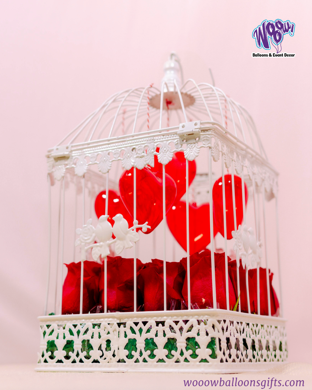 Lovebird Rose Cage with fresh red roses inside a vintage-inspired white birdcage with heart decorations.