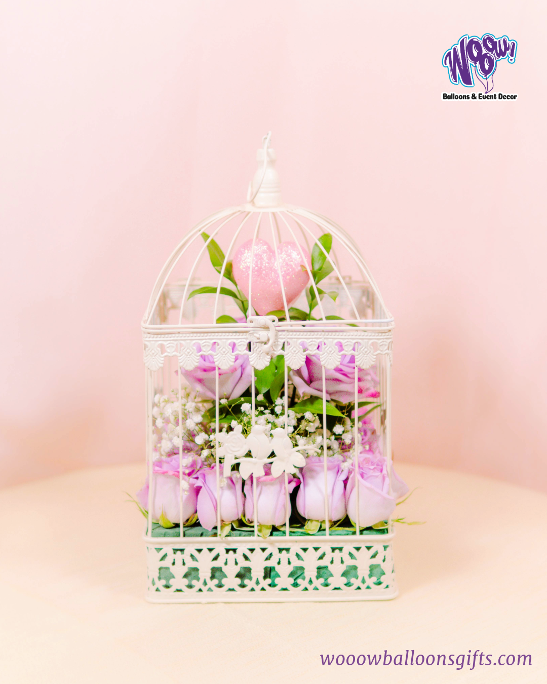 Enchanted Love Cage with fresh lavender roses and a sparkling pink heart inside a white decorative birdcage.