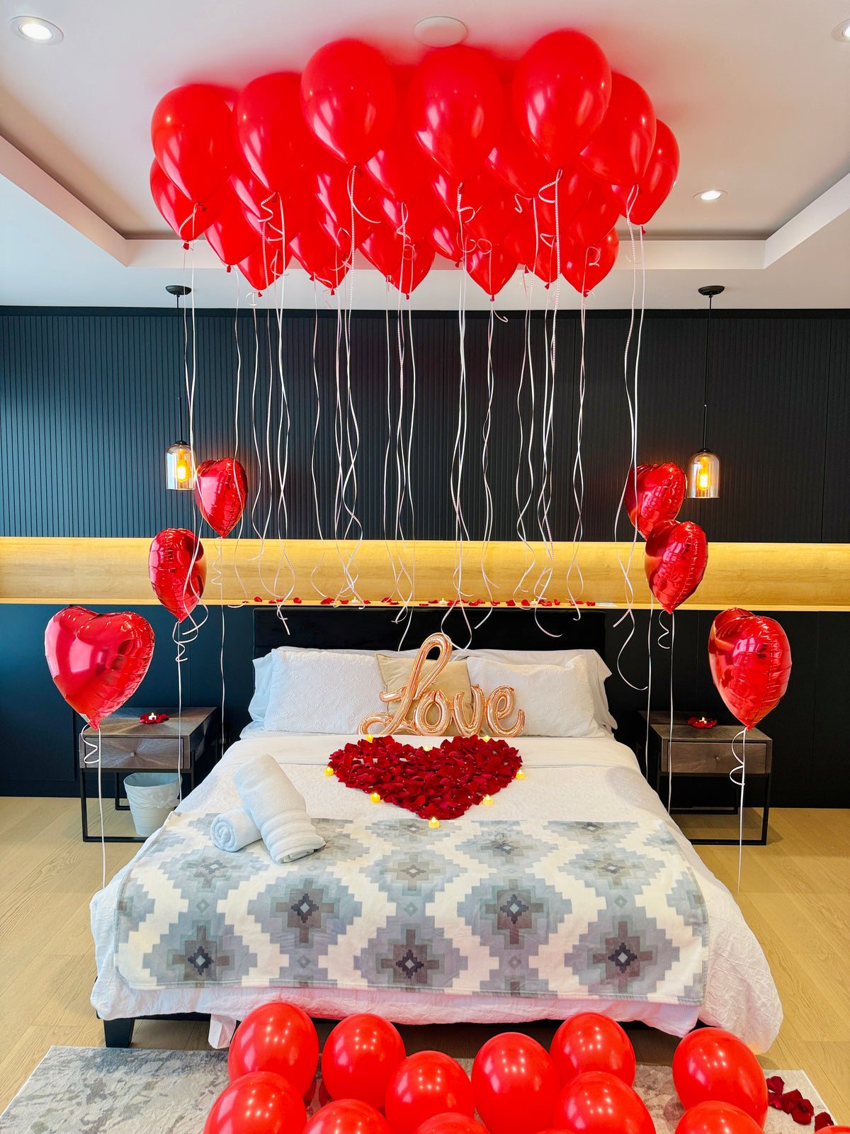 Anniversary room decor with red heart balloons rose petals and warm LED candles in Toronto