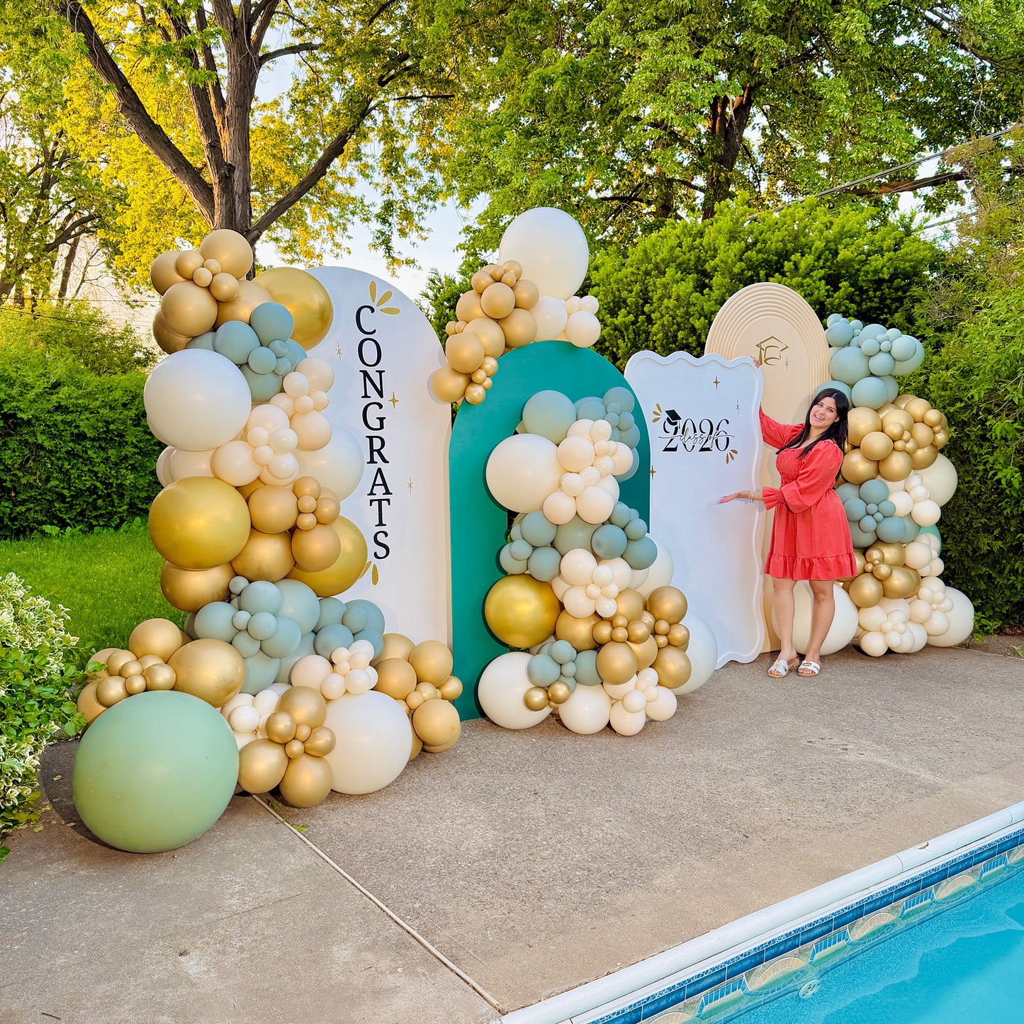 Decorative balloon arch with 'Congrats' and '2026' signs, outdoors by a pool.