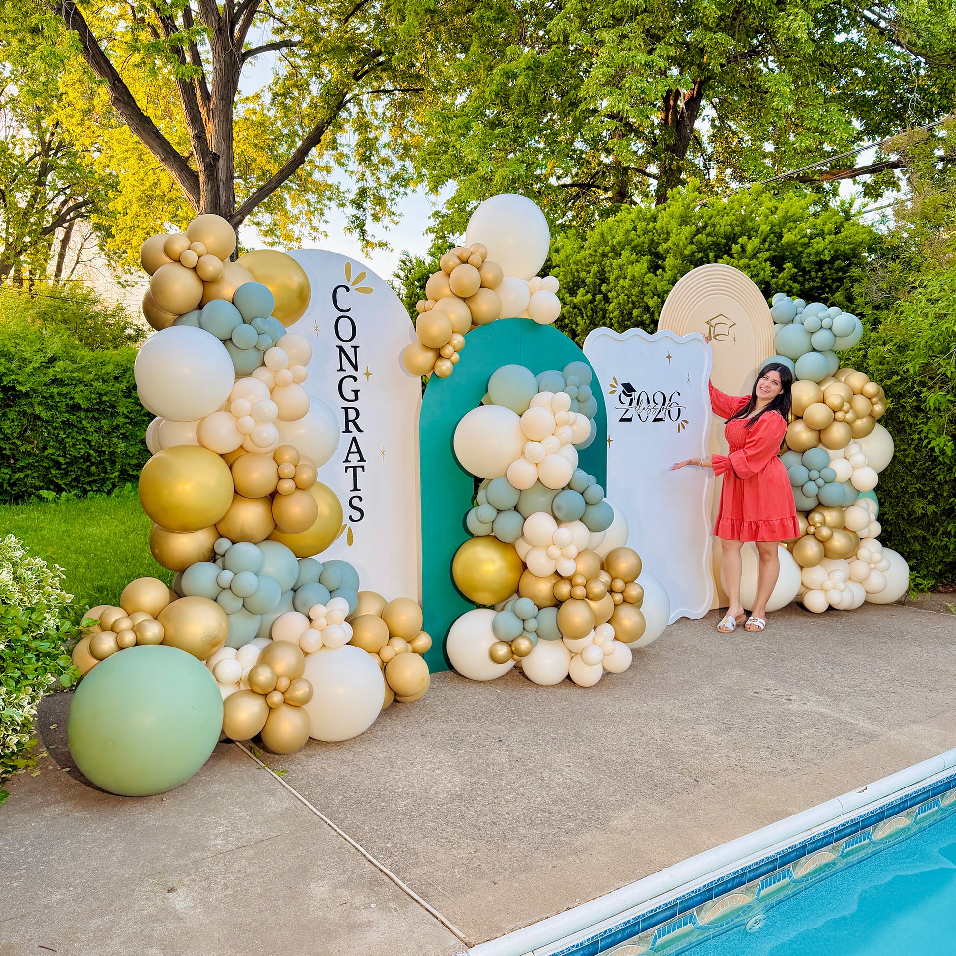 Decorative balloon arch with 'Congrats' and '2026' signs, outdoors by a pool.