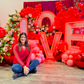 Luxury 'LOVE' marquee letter balloon installation with red and blush balloon garlands, floral accents, and oversized metallic mirror balls. A woman poses in front of the display.