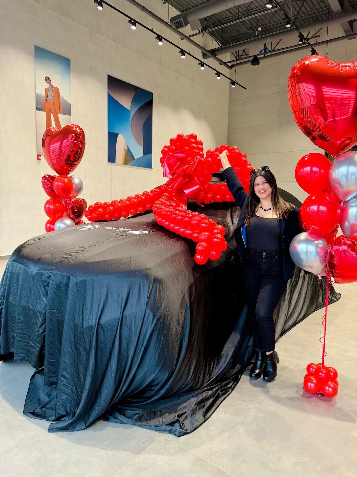 Luxury BMW car reveal setup with an oversized red balloon bow and red and silver heart bouquets in Toronto.