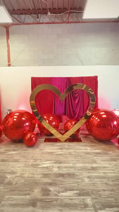 Valentine’s Day balloon setup with a gold heart frame, red balloon clusters, floral decor, and mirror balls.
