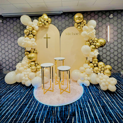 Decorative arch with balloons and a cross on a patterned wall.
